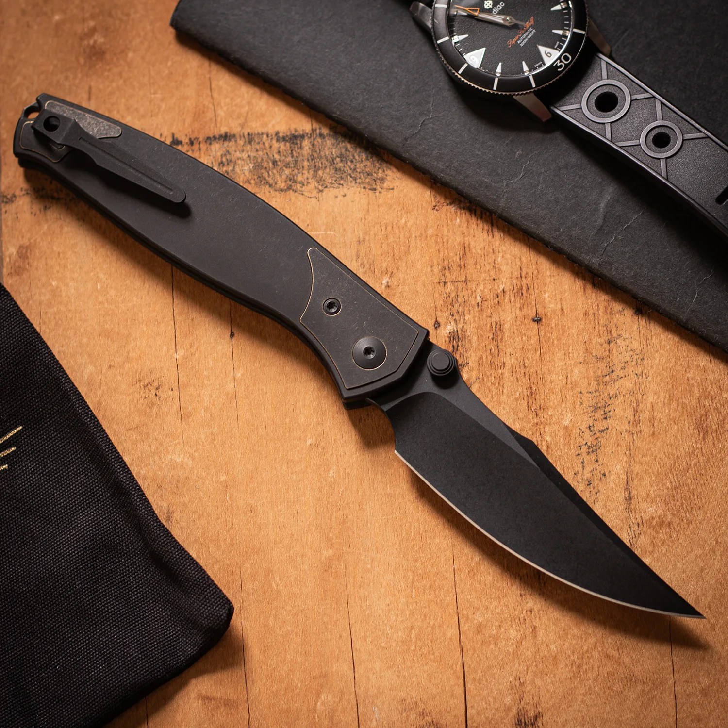 Black folding knife with a clip and a partially serrated blade on a wooden surface.