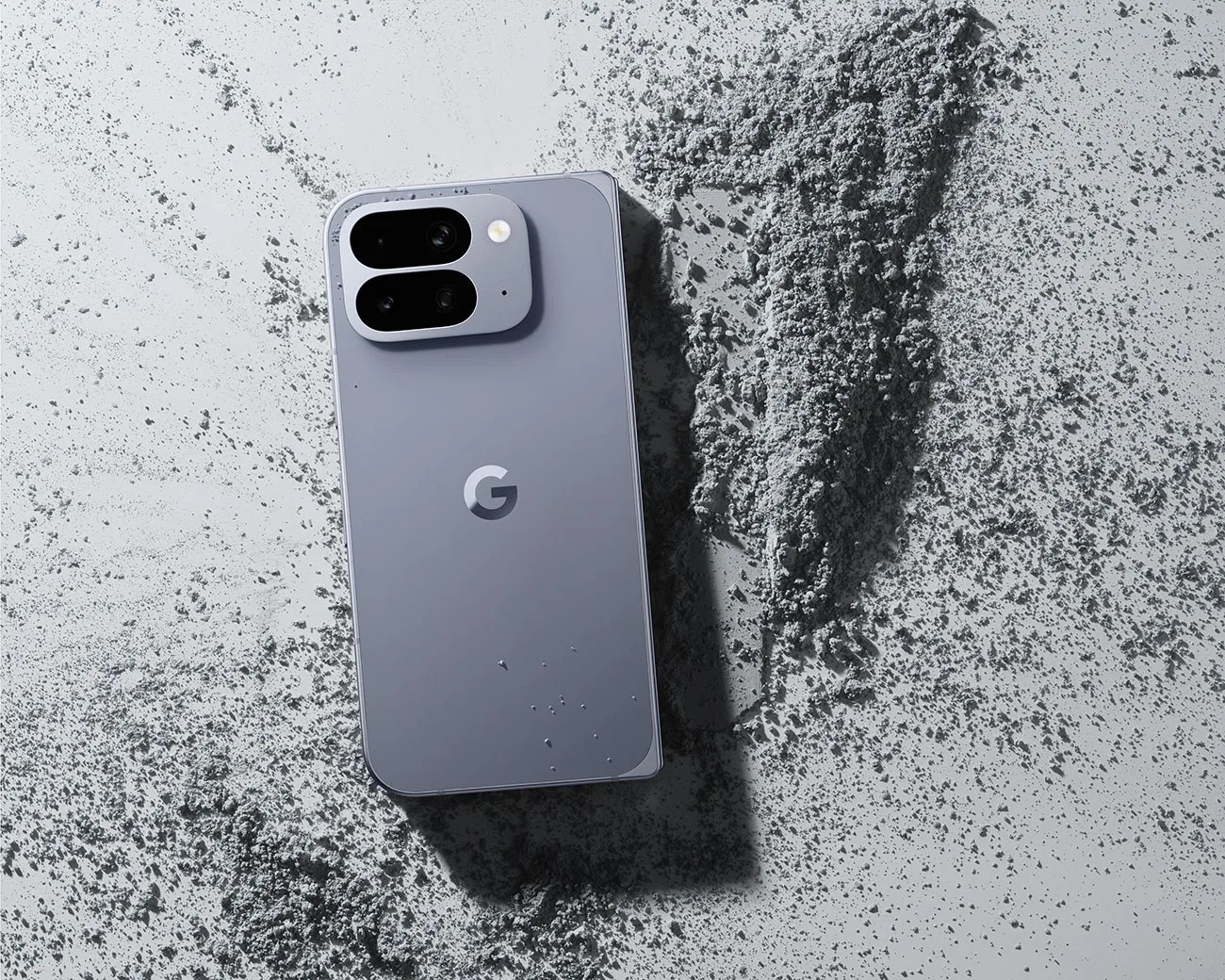 Gray Google smartphone with dual rear cameras lying on a surface with scattered gray powder.