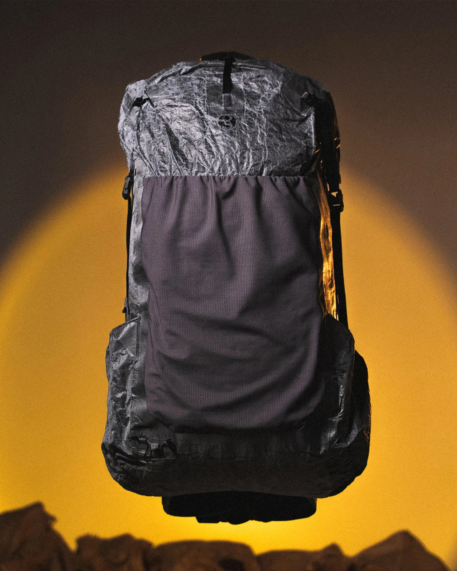 Black and gray textured backpack with a large front pocket, suspended against a yellow-orange background.