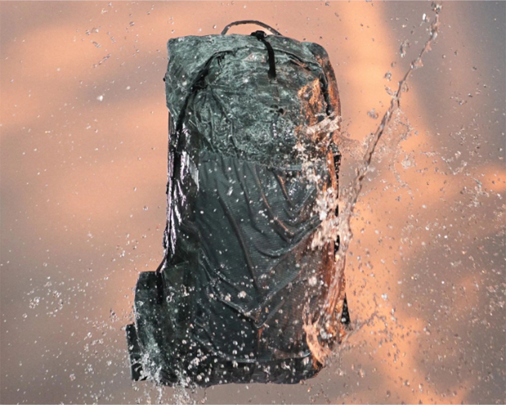 Dark green backpack splashed with water droplets against a blurred orange background.