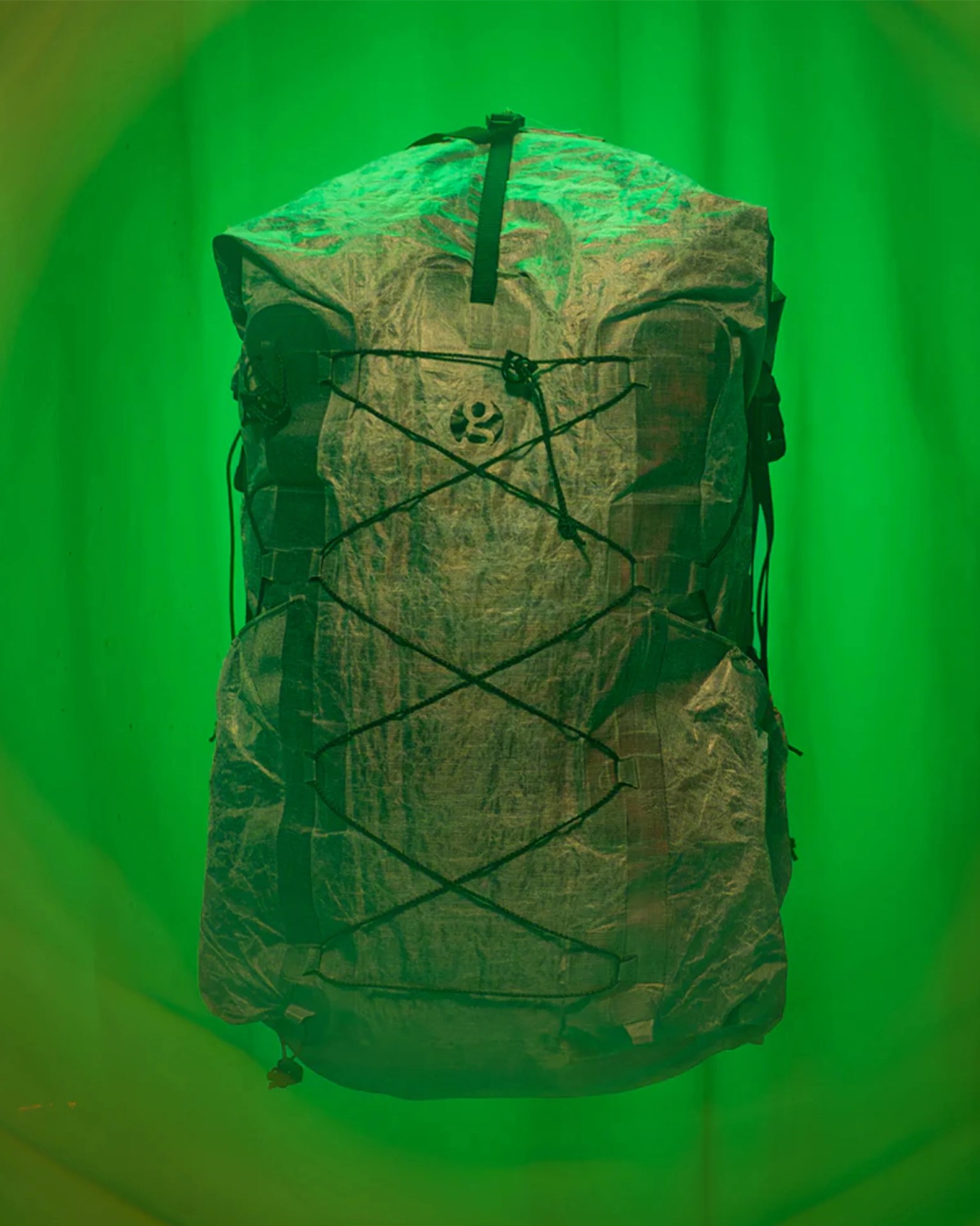 Lightweight gray backpack with black straps and bungee cord on a green background.