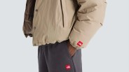 Beige puffer jacket and dark gray pants with red The North Face logo patches.