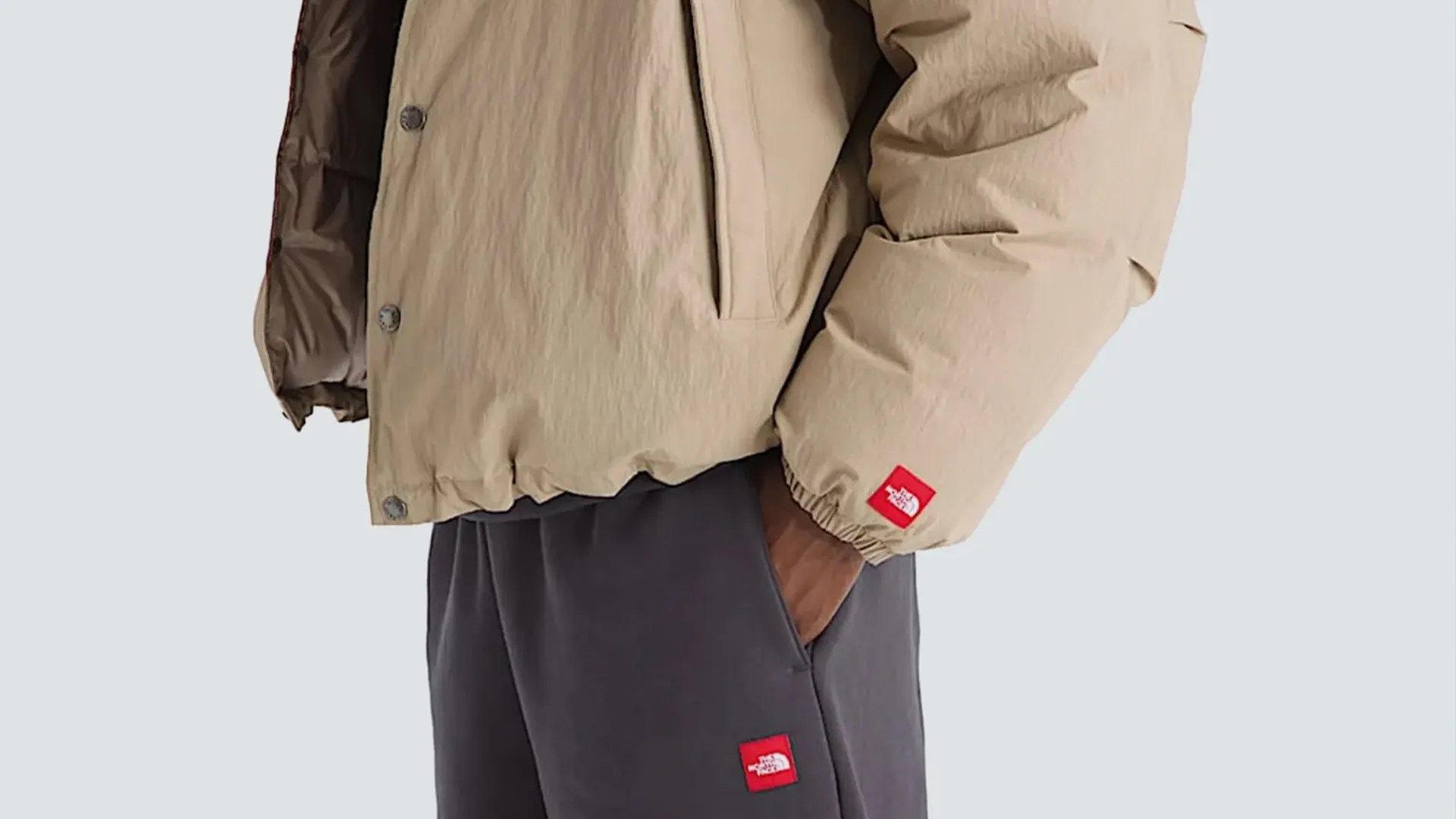 Beige puffer jacket and dark gray pants with red The North Face logo patches.