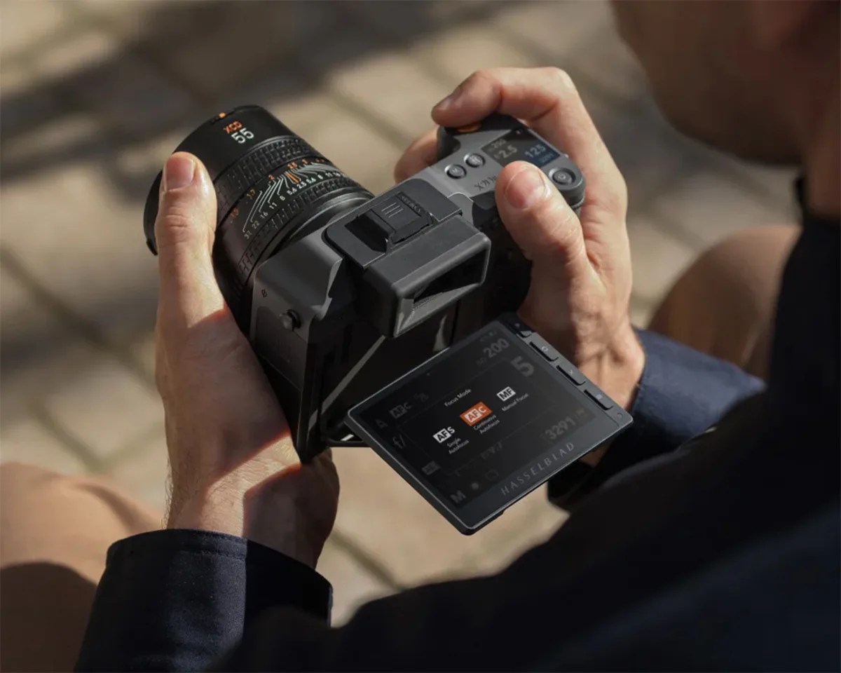Person holding a Hasselblad camera with a 55mm lens and a tilted LCD screen showing autofocus settings.