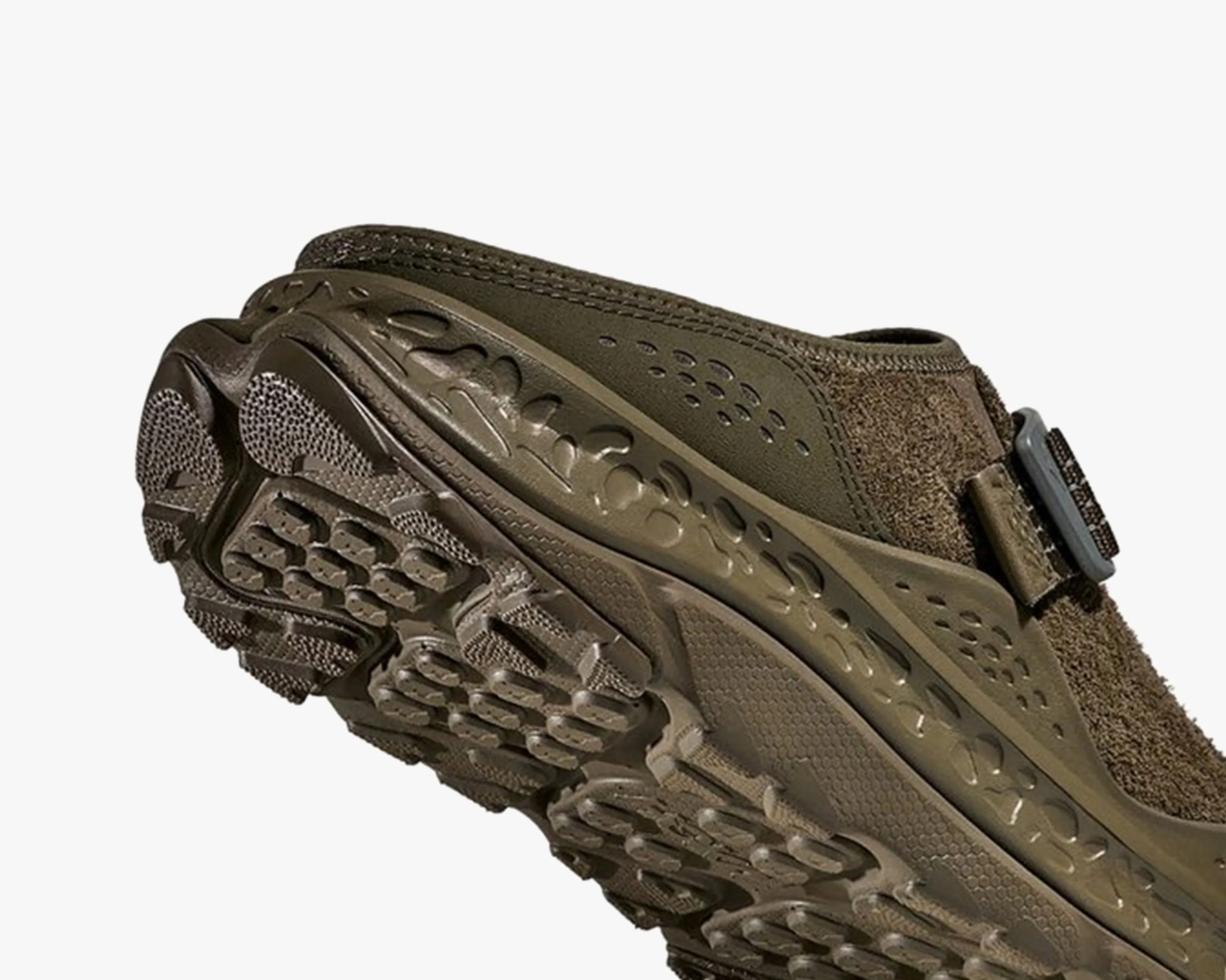 Close-up of the sole and side of an olive green outdoor shoe with textured tread and a buckle strap.