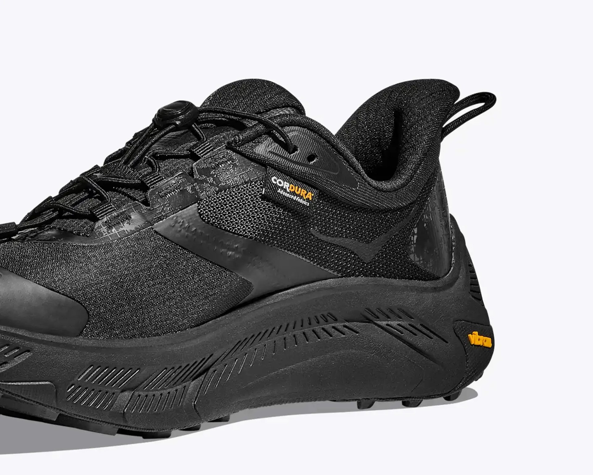Black athletic shoe with Cordura fabric tag and Vibram sole logo in orange.