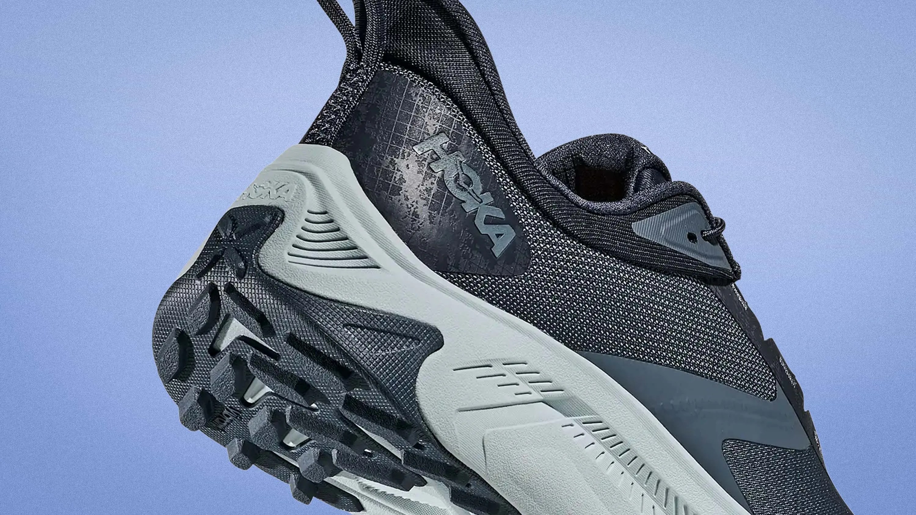 Black and gray Hoka running shoe with textured sole and mesh upper against a blue background.