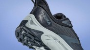 Black and gray Hoka running shoe with textured sole and mesh upper against a blue background.
