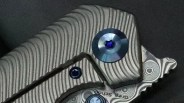 Close-up of a textured metal knife handle with blue screws and a patterned metal base.