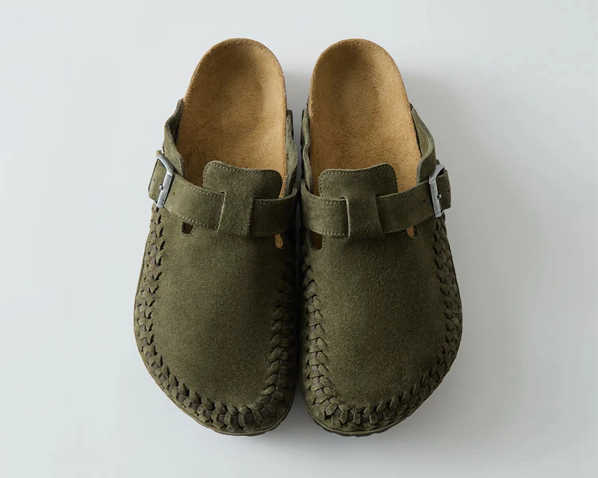 Pair of olive green suede slip-on clogs with woven edges and adjustable buckle straps.