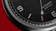 Close-up of a black watch dial showing silver hour markers, a red second hand, and text reading "AUTOMATIC 100M=330ft.