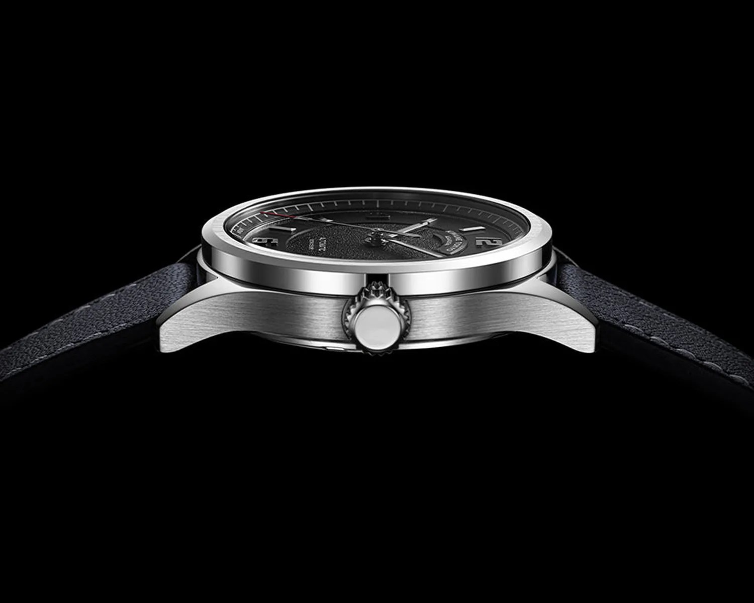 Side view of a silver stainless steel wristwatch with a black textured dial and black leather strap on a black background.