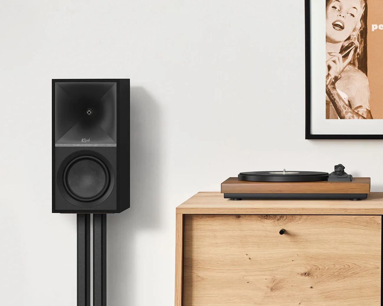 Black Klipsch speaker on a black stand next to a wooden cabinet with a turntable on top.