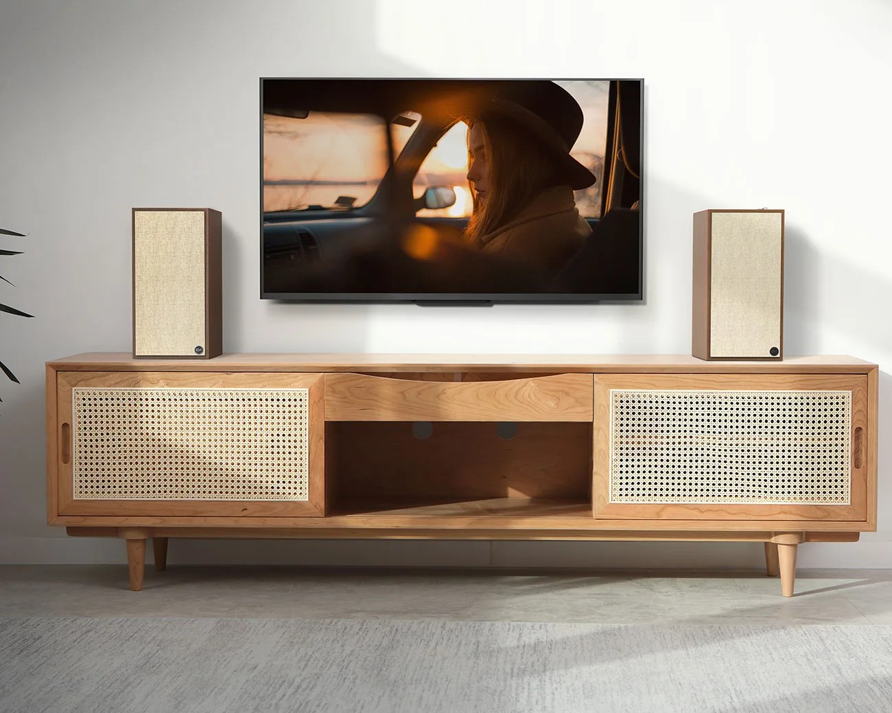 Light wood TV stand with woven cane sliding doors and two beige speakers on top, beneath a wall-mounted flat screen TV.
