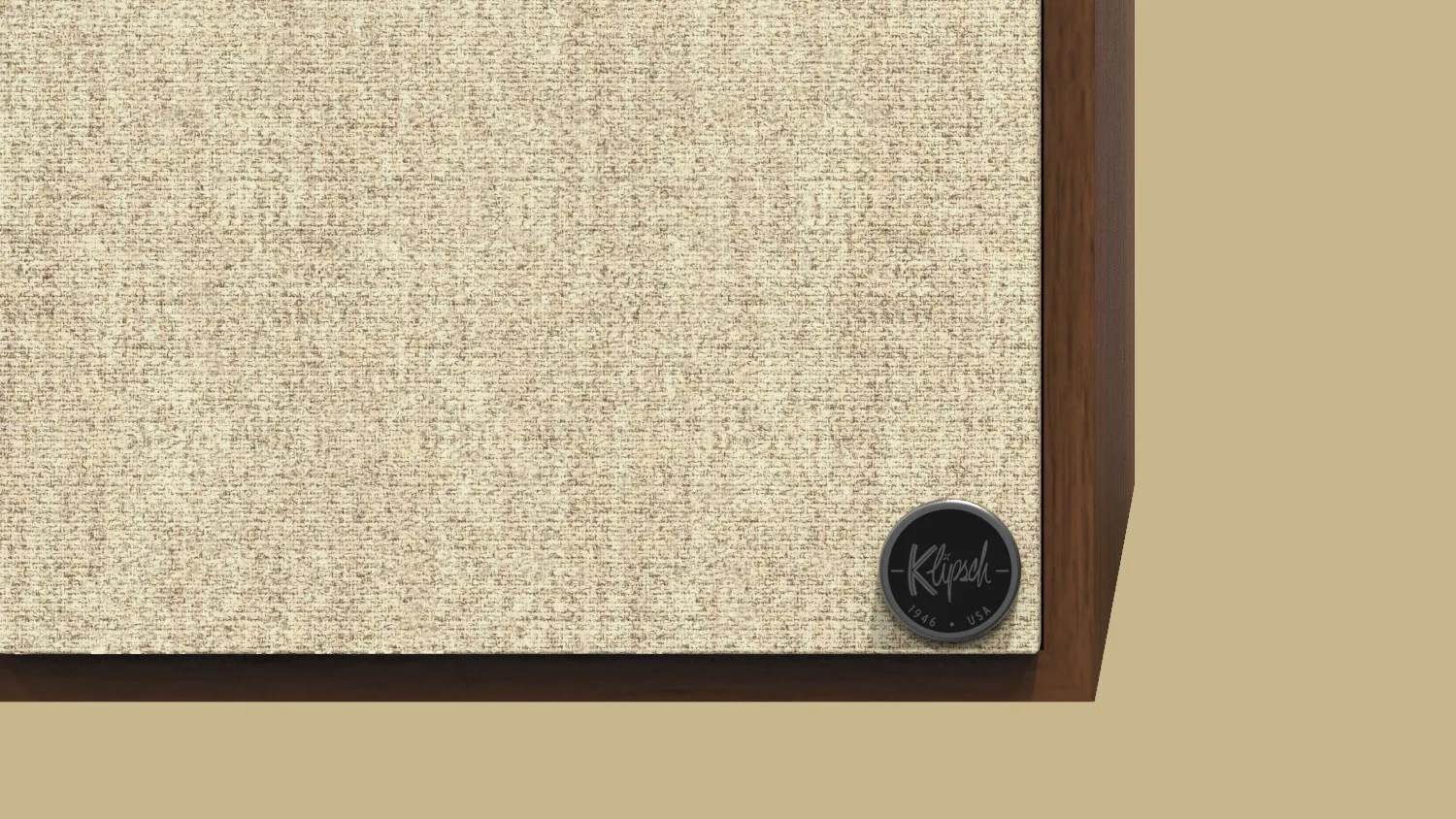 Close-up of a beige fabric speaker grille with a round black Klipsch logo badge on a wooden frame.