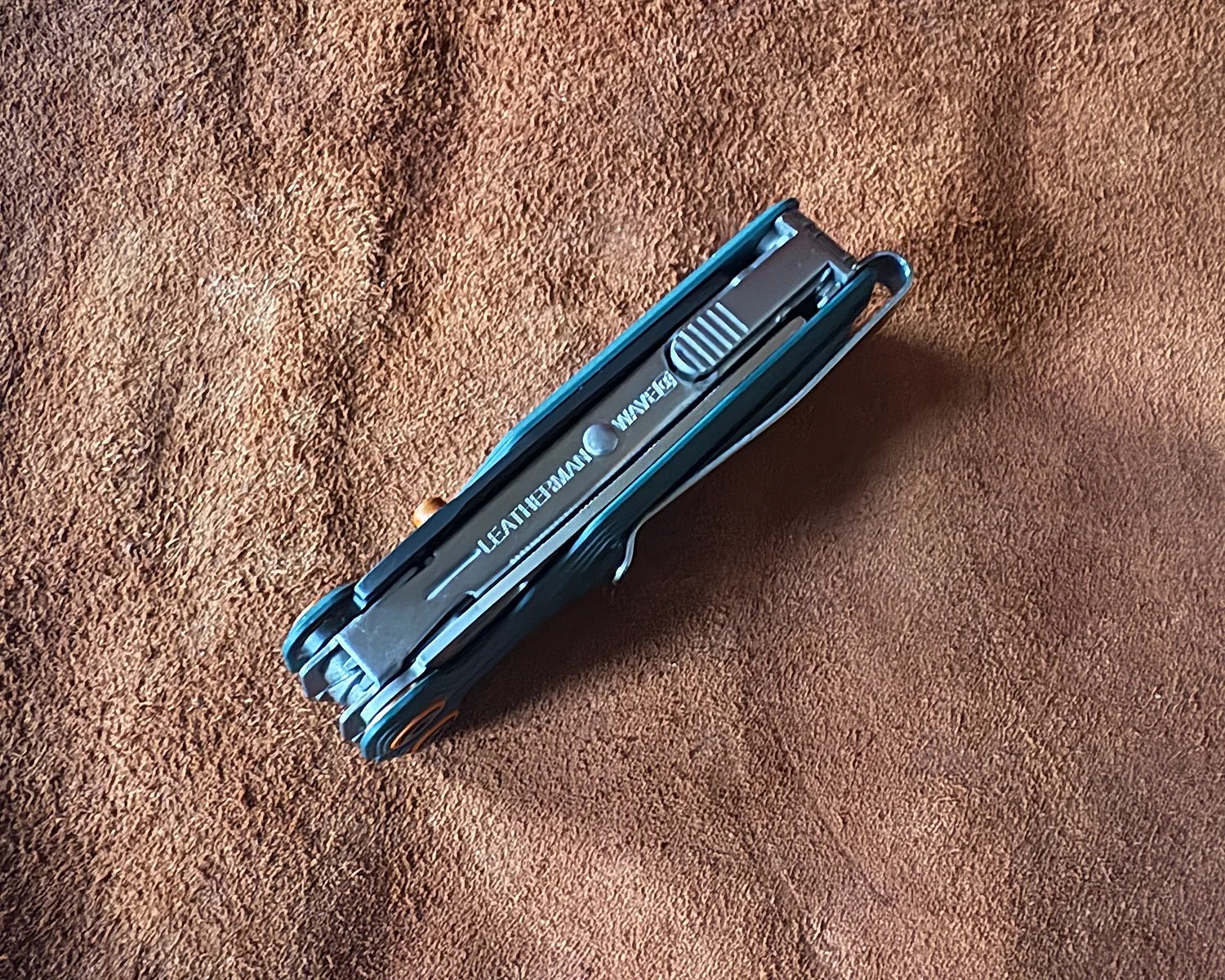Folded black Leatherman Wave multi-tool on a brown textured surface.