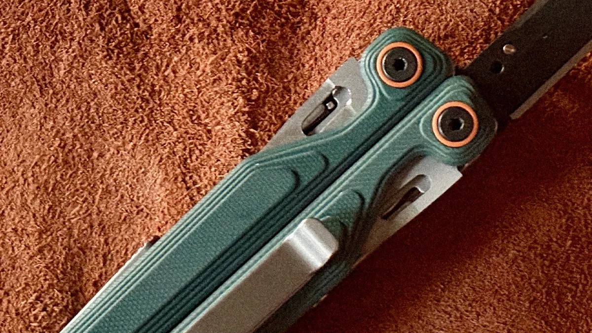 Close-up of a green textured butterfly knife handle with copper-colored washers on a brown fabric background.