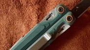 Close-up of a green textured butterfly knife handle with copper-colored washers on a brown fabric background.