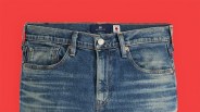 Blue denim jeans with faded whiskering and a button fly on a red background.