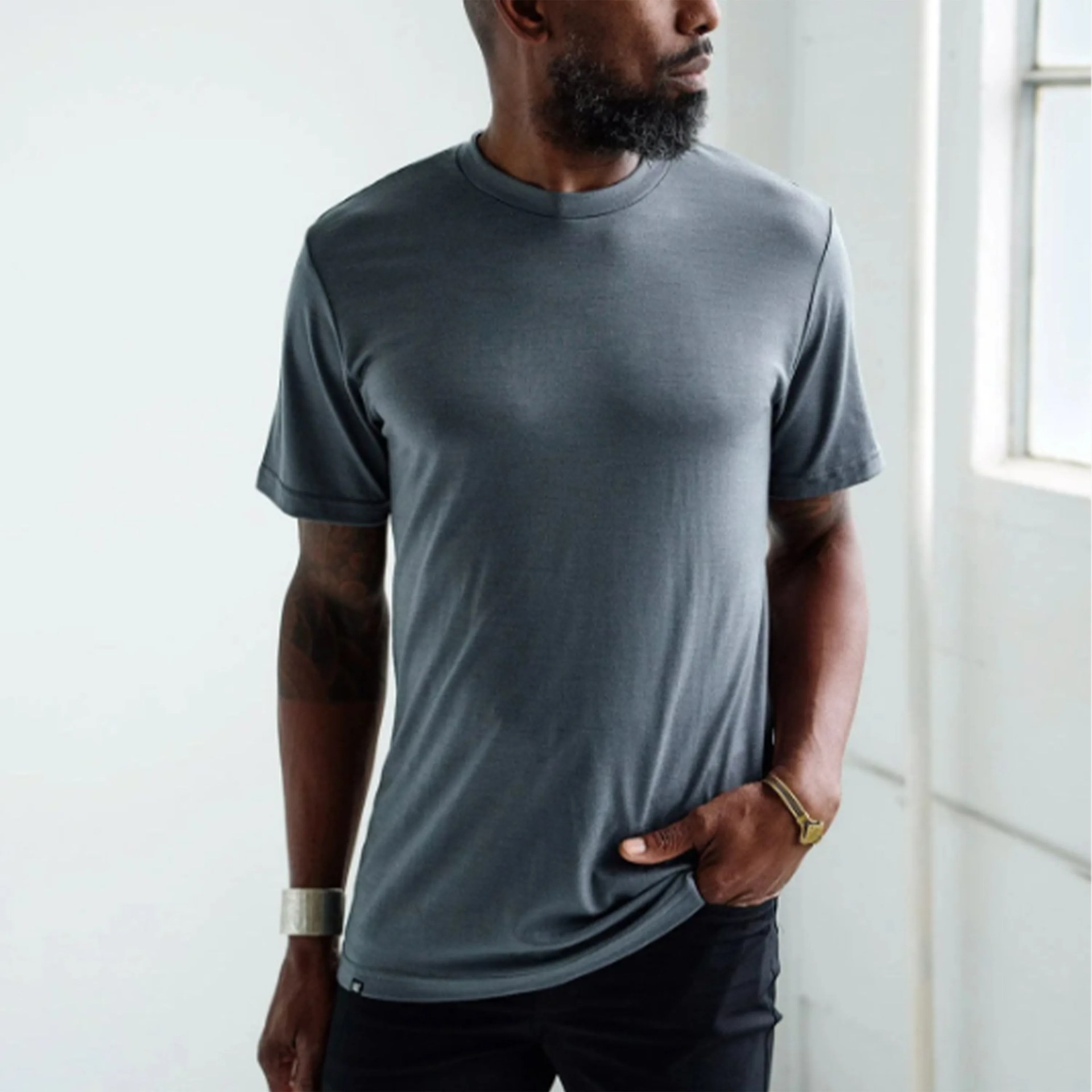 Fitted dark gray short-sleeve crew neck t-shirt worn by a person with one hand in pocket.