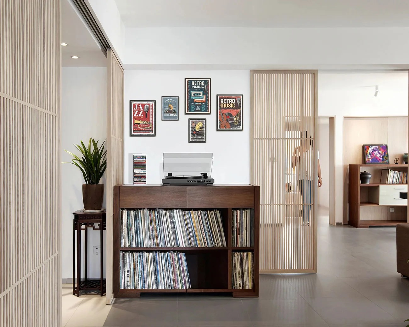 Dark wood record cabinet filled with vinyl records and a turntable on top, set against a white wall with framed retro music posters.