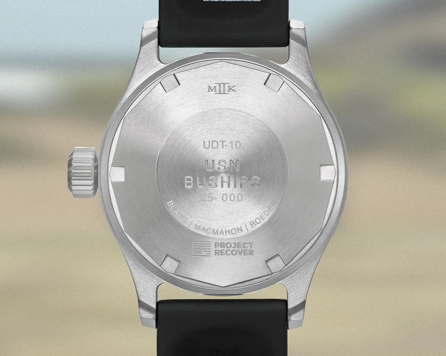 Brushed stainless steel watch back with engravings including "UDT-10 USN BUSHIPS 25-000" and "PROJECT RECOVER" on a black strap.