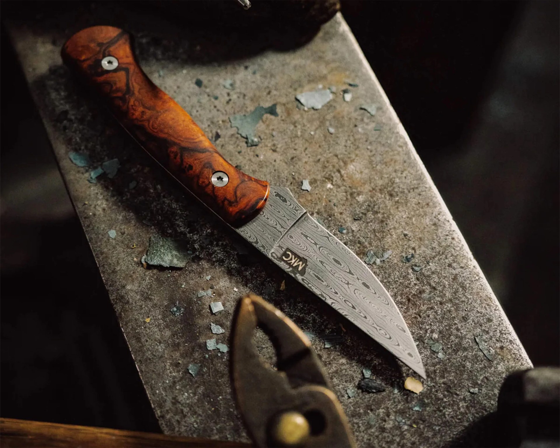 Knife with a patterned steel blade and a polished wooden handle resting on a rough metal surface.