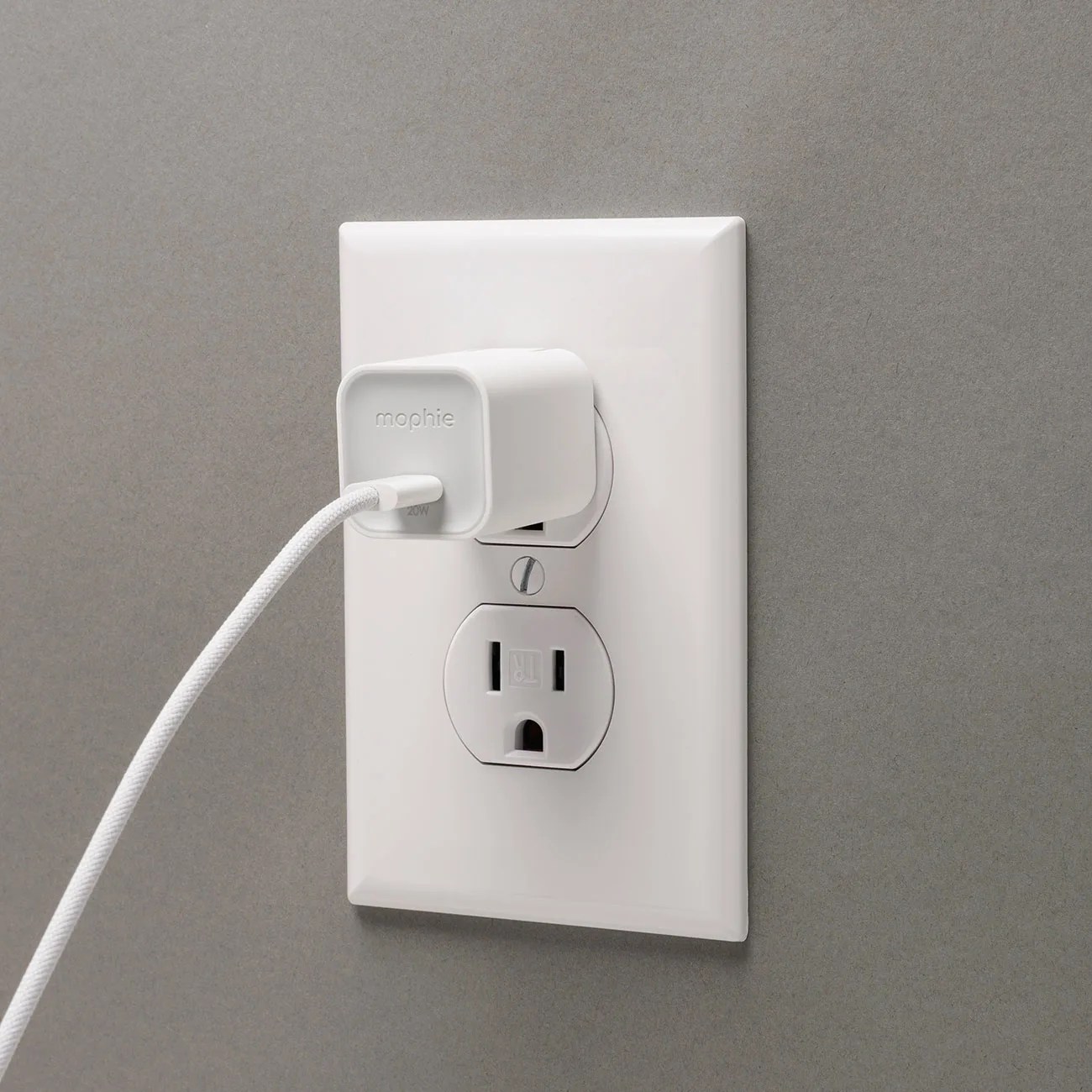 White Mophie 20W USB-C wall charger plugged into a white electrical outlet on a gray wall.
