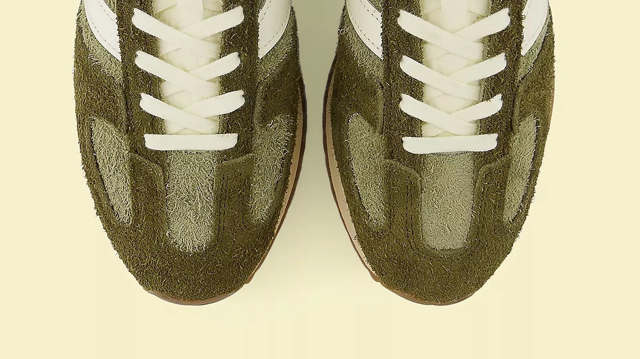 Pair of olive green suede sneakers with white laces and white side stripes on a light background.