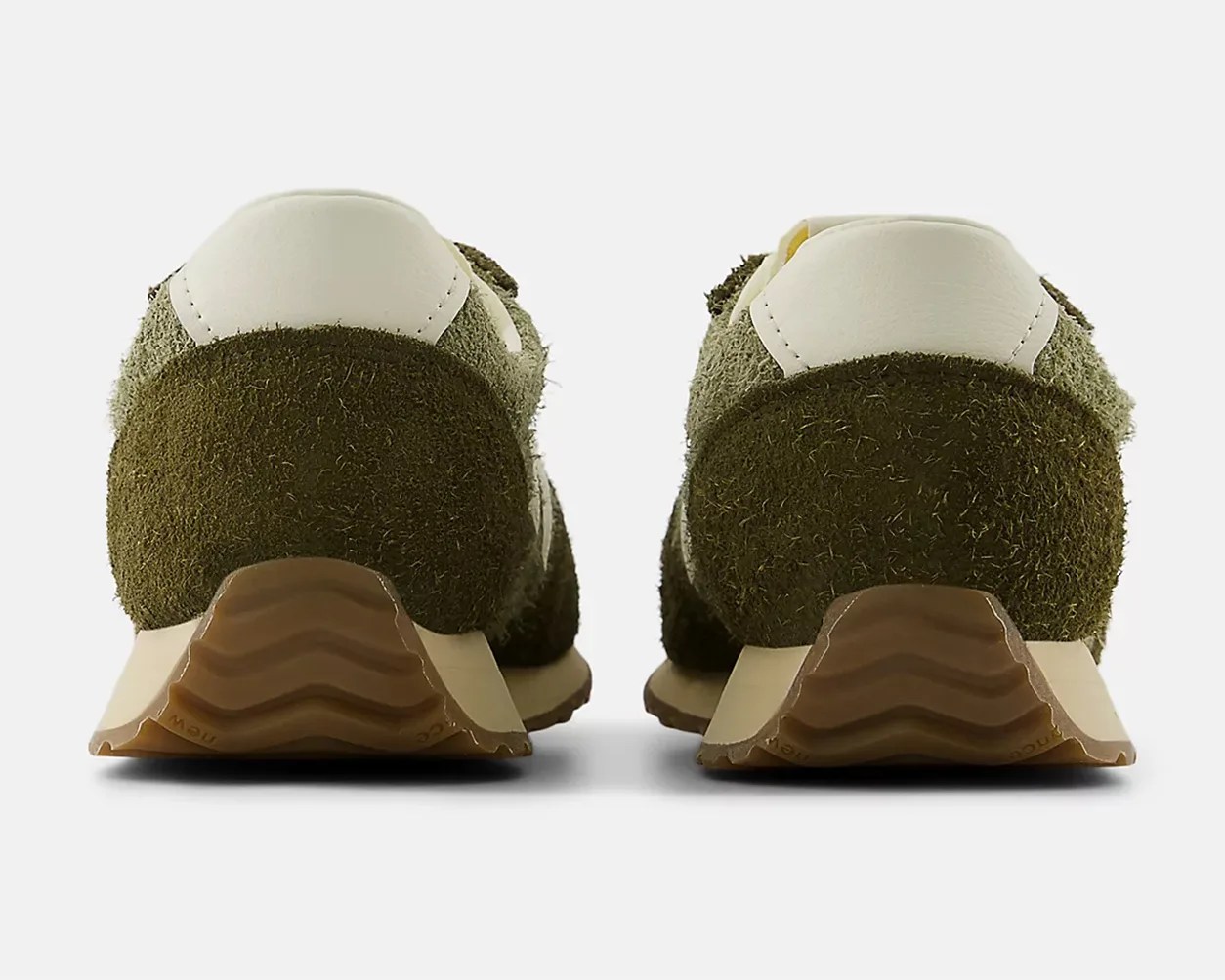 Pair of olive green suede sneakers with white leather heel tabs and brown rubber soles, viewed from the back.