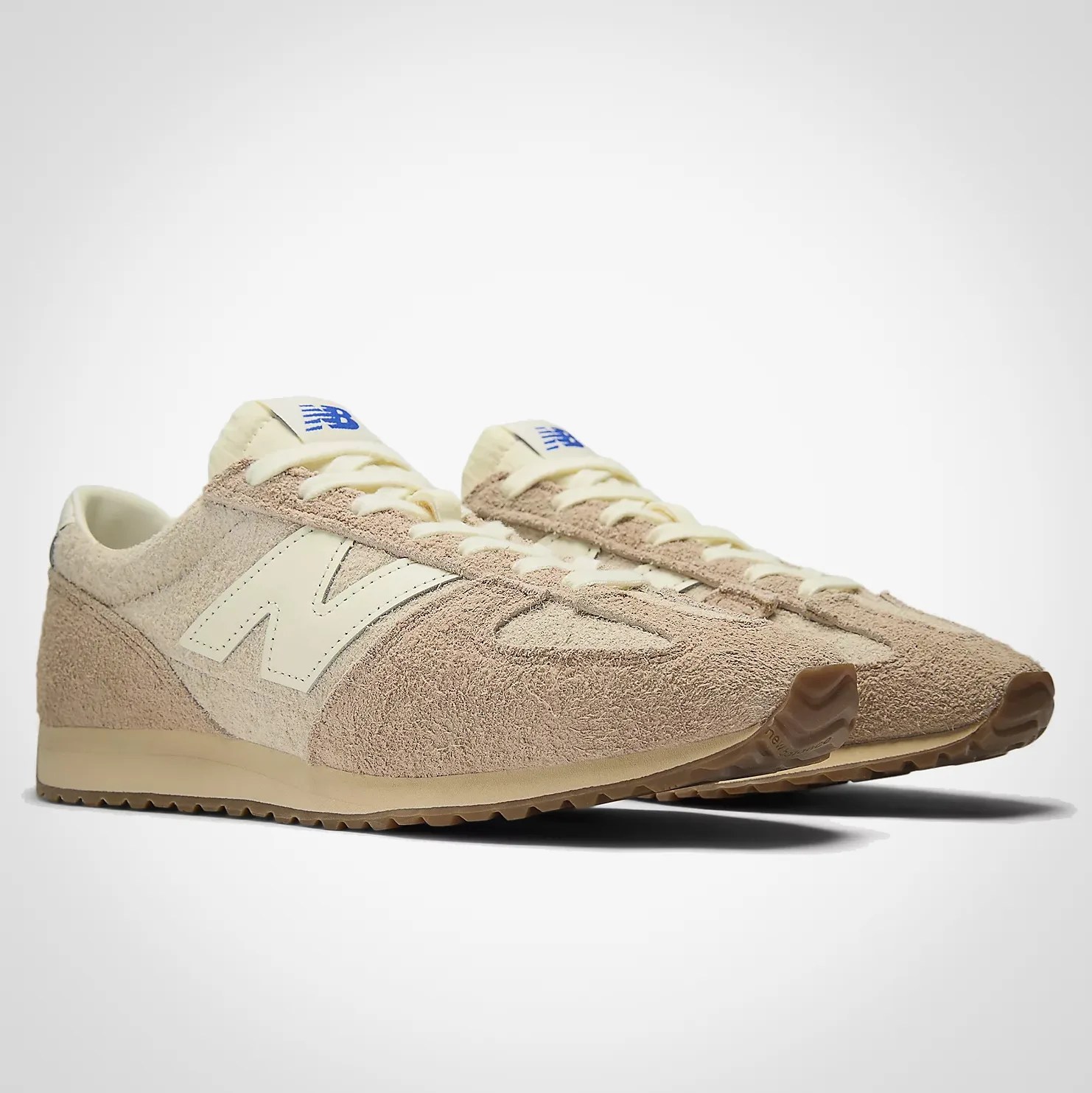 Pair of beige New Balance suede sneakers with cream laces and blue logo on the tongue.