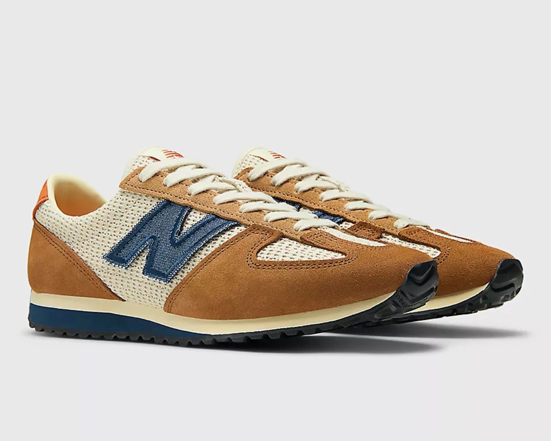Pair of brown suede and cream mesh New Balance sneakers with blue logo and black soles.