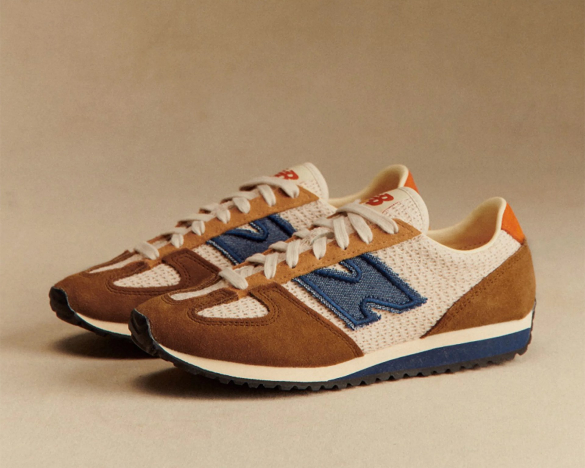 Pair of brown and beige New Balance sneakers with blue logo and white laces on a beige background.