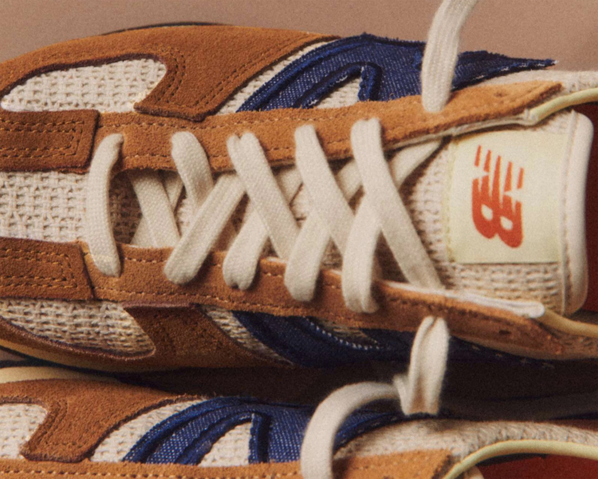 Close-up of brown suede and beige mesh New Balance sneakers with white laces and blue accents.