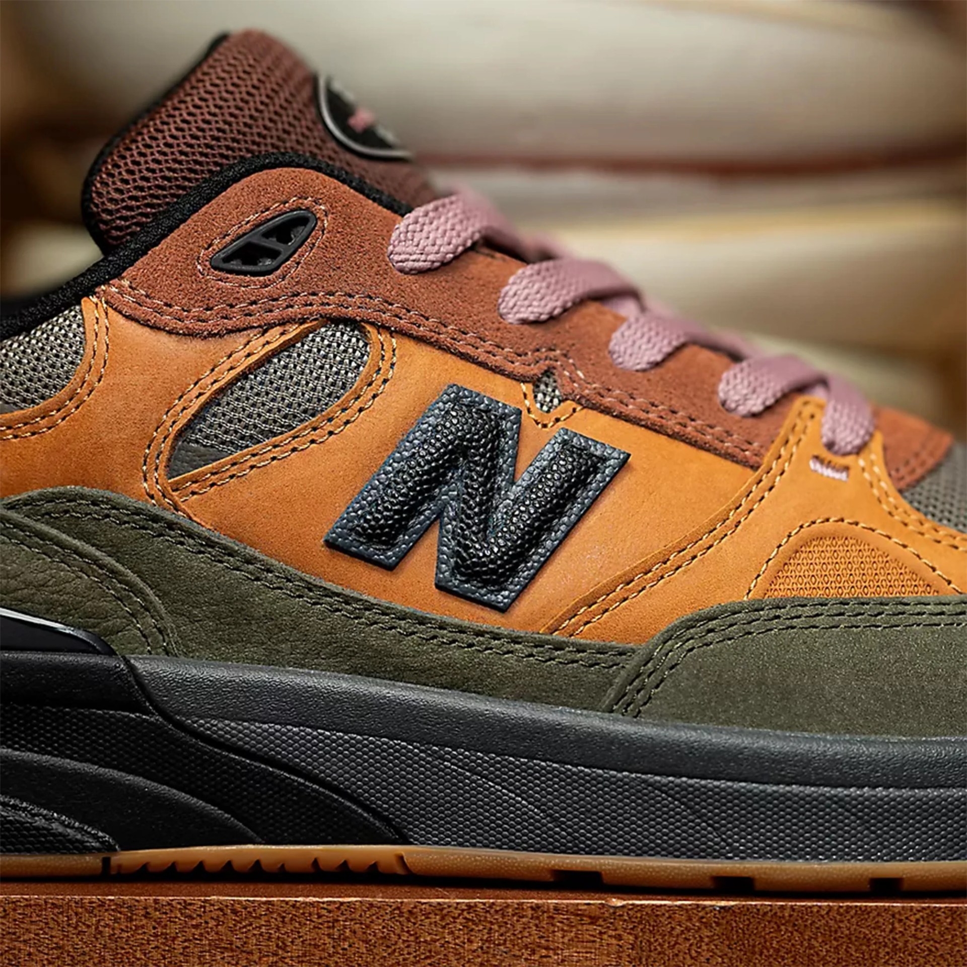 Close-up of a New Balance sneaker with brown, orange, olive green suede, and pink laces.