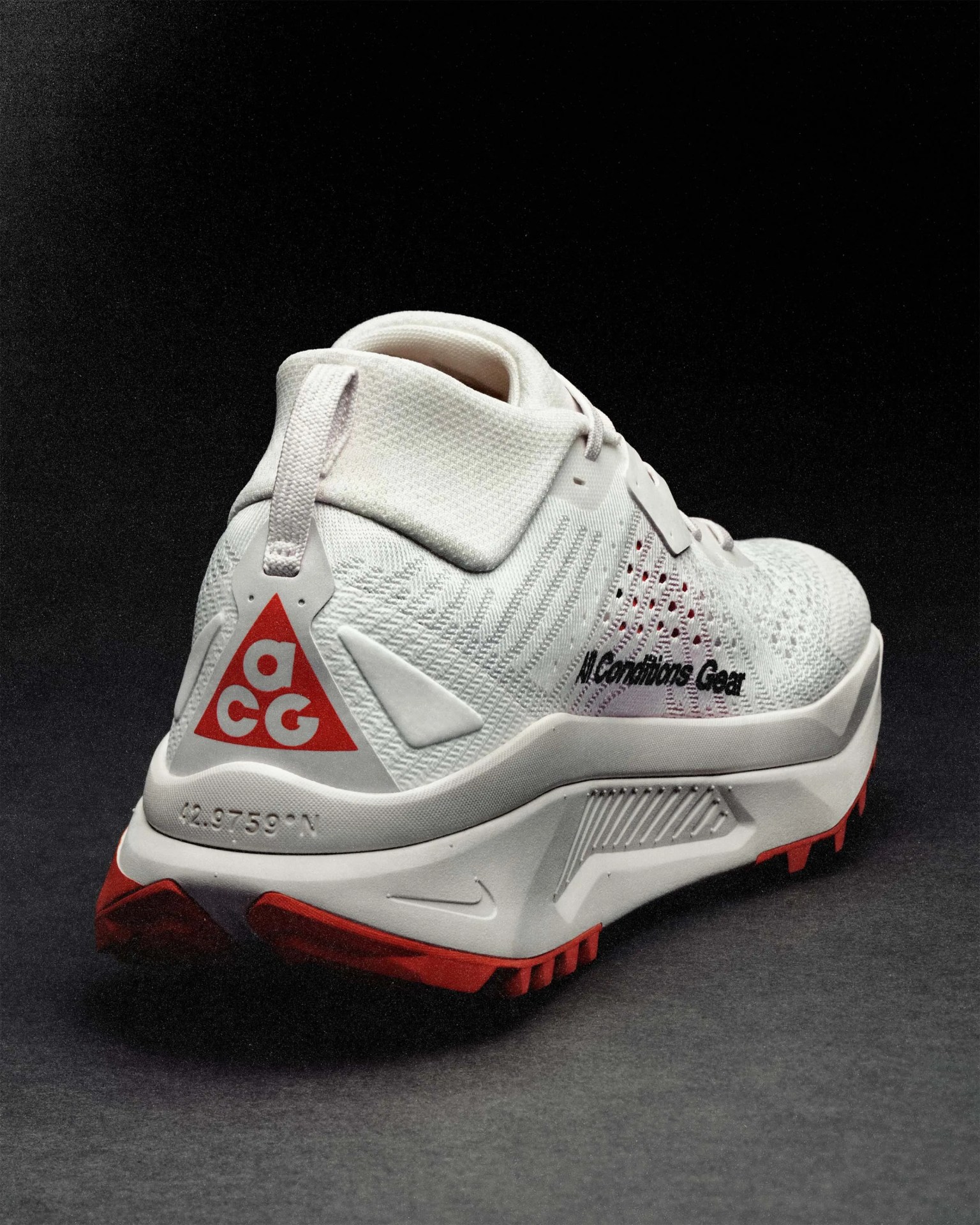 White Nike ACG sneaker with red accents and textured sole on a dark surface.