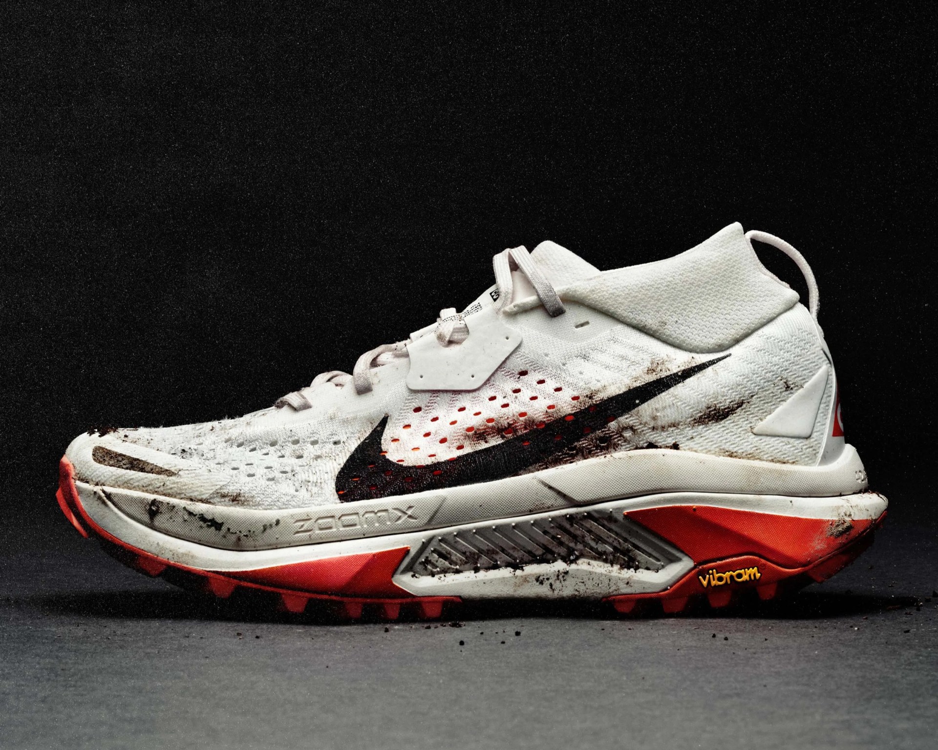 White Nike ZoomX running shoe with black swoosh and red Vibram sole, showing dirt stains.
