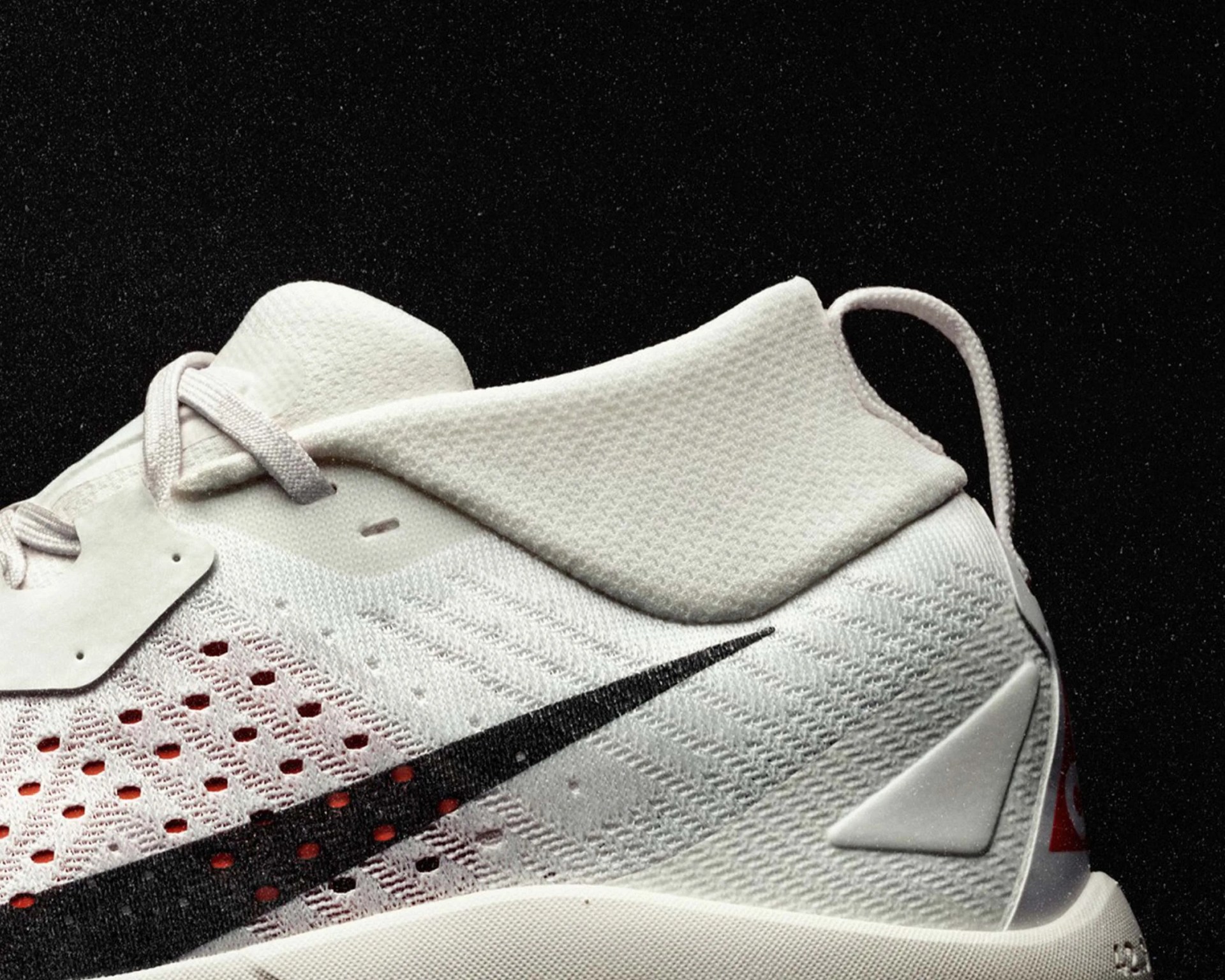 Close-up of a white Nike sneaker with black swoosh and textured knit upper on a black background.