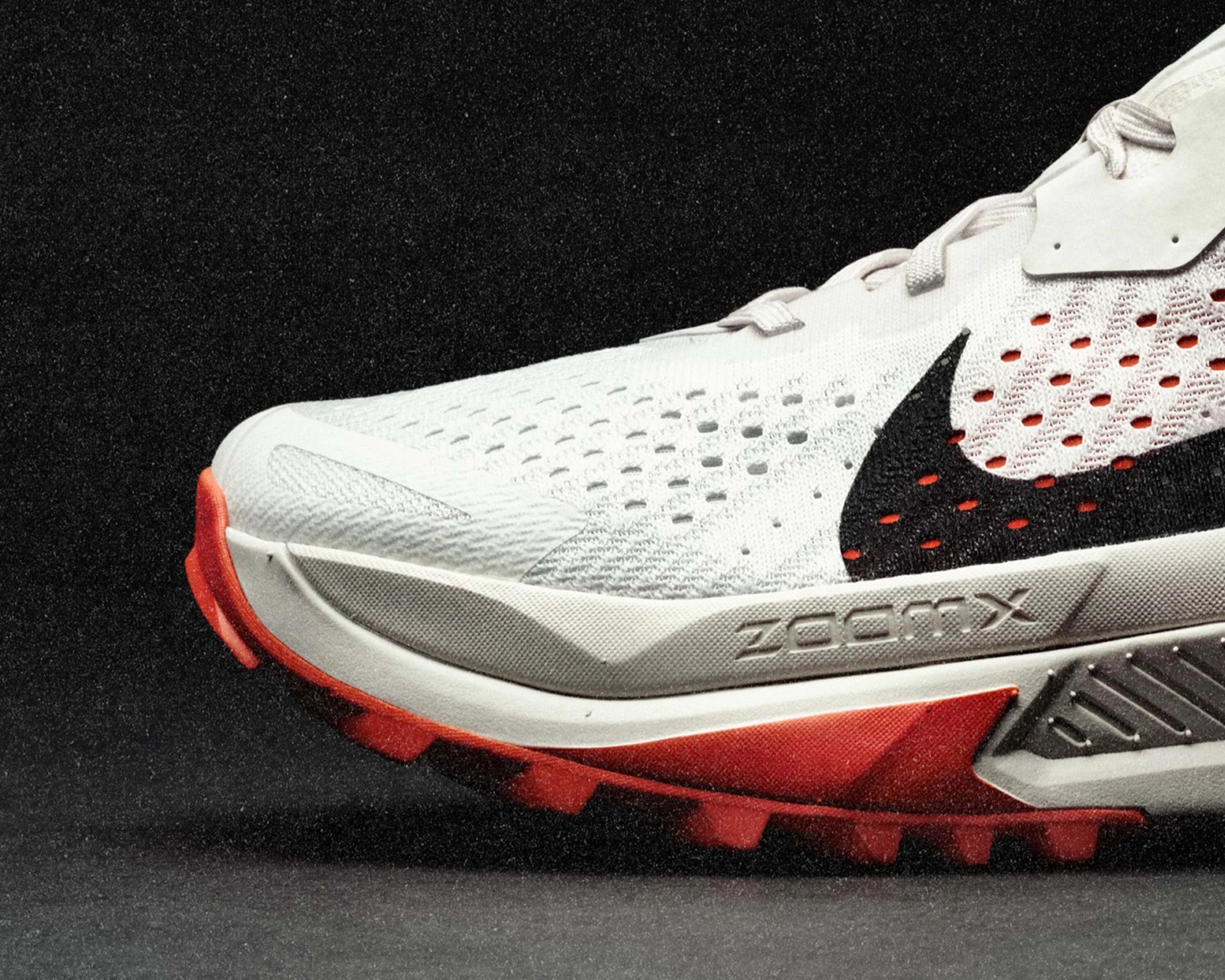 Close-up of a white Nike ZoomX running shoe with black swoosh and red outsole on a dark surface.