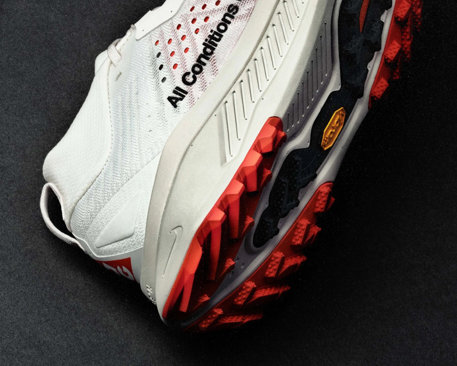 White athletic shoe with red and black rugged sole and "All Conditions" text on the side.