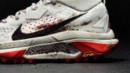 White and red Nike ZoomX running shoe with black swoosh and Vibram sole, showing dirt marks.