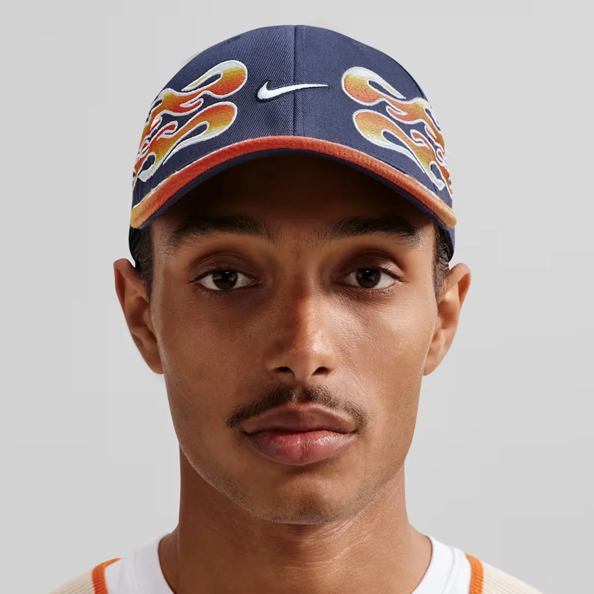 Navy blue Nike cap with orange flame designs worn by a person against a gray background.