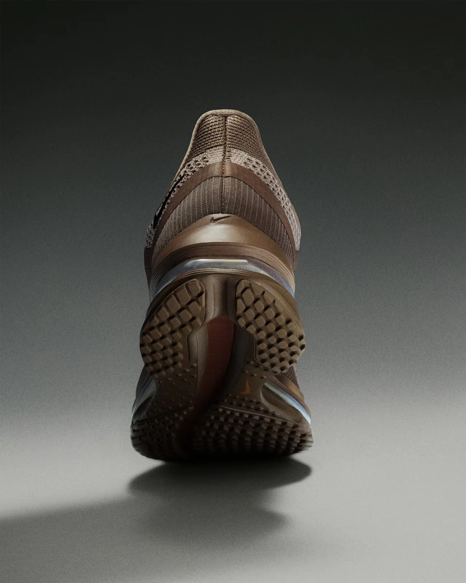 Brown Nike running shoe with textured sole viewed from the back against a gradient gray background.