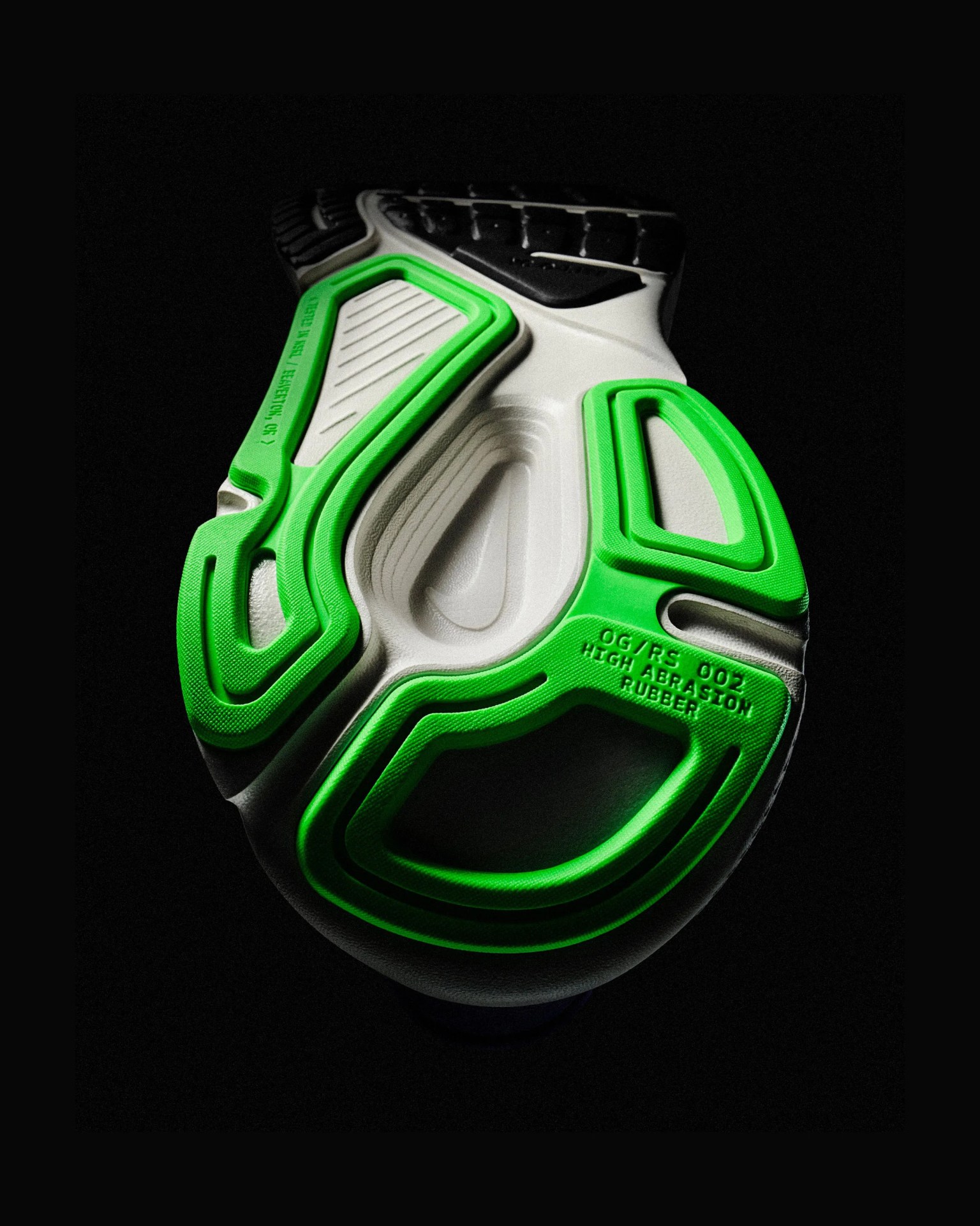 Sole of a sneaker with white base and bright green high abrasion rubber accents on a black background.