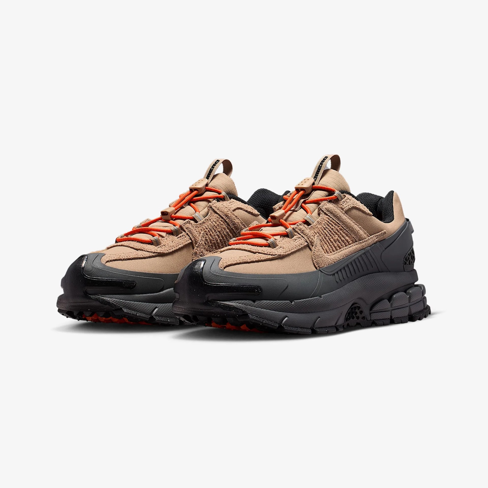 Pair of tan and black athletic shoes with orange laces and thick textured soles on a white background.