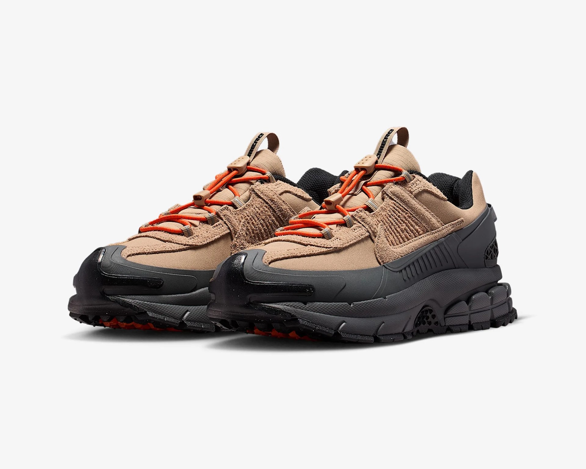 Pair of tan and black sneakers with orange laces and rugged black soles on a white background.
