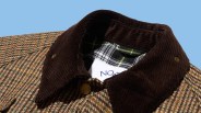 Brown corduroy collar on a multicolored houndstooth patterned jacket with a plaid inner lining.