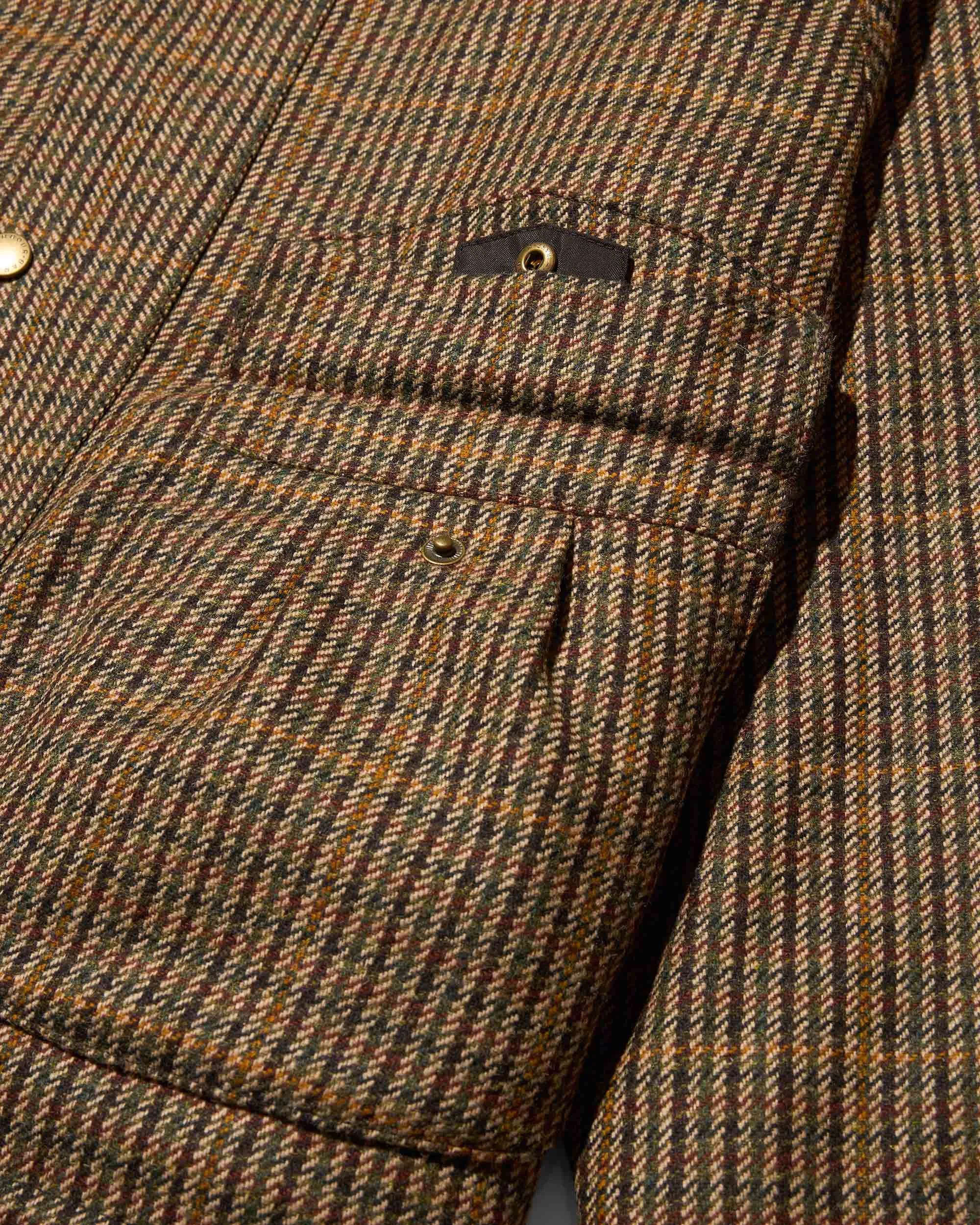 Close-up of brown, green, and orange houndstooth patterned wool jacket pocket with brass snap button.
