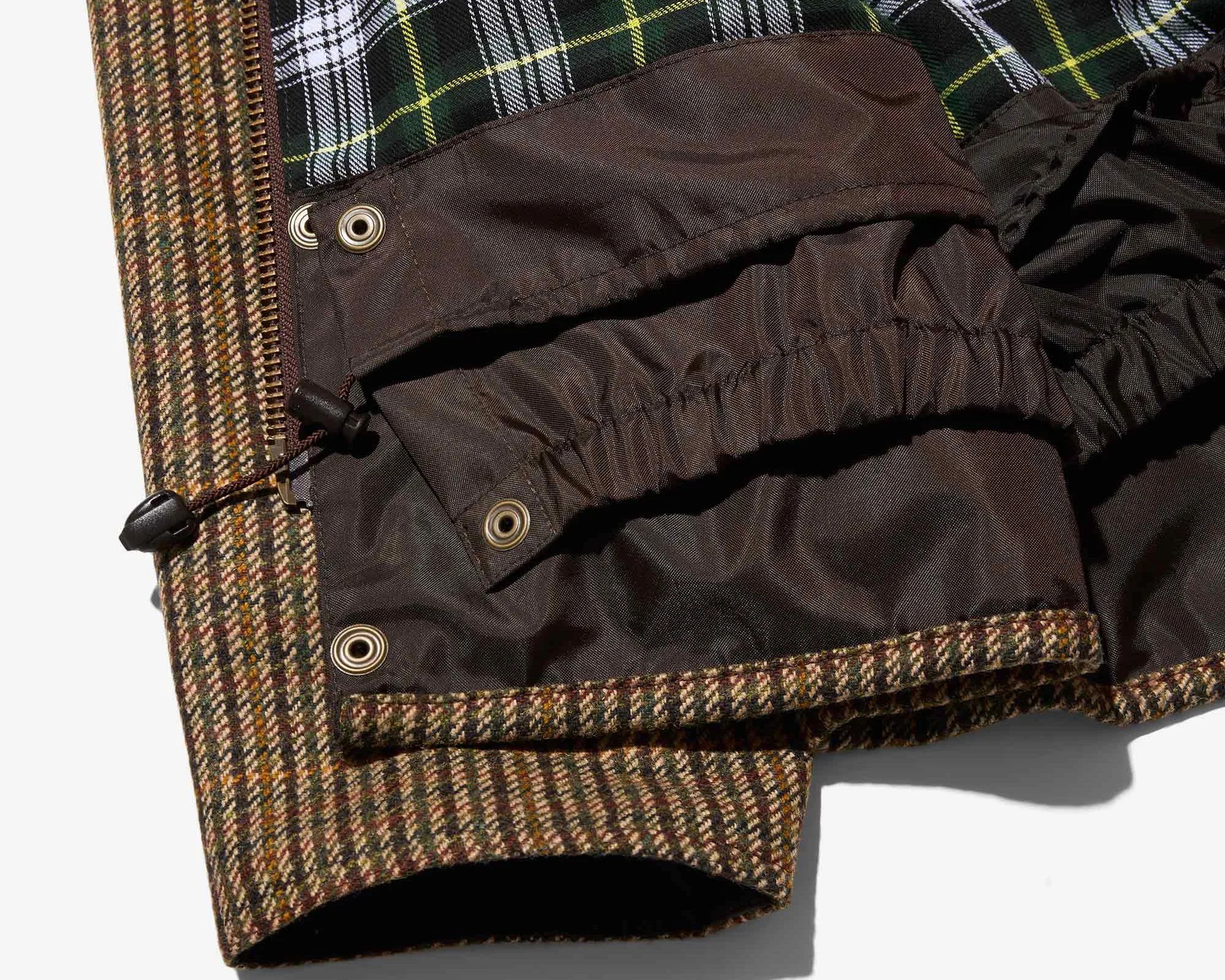 Close-up of a brown tweed jacket hem with a dark brown inner lining featuring elastic and snap buttons.