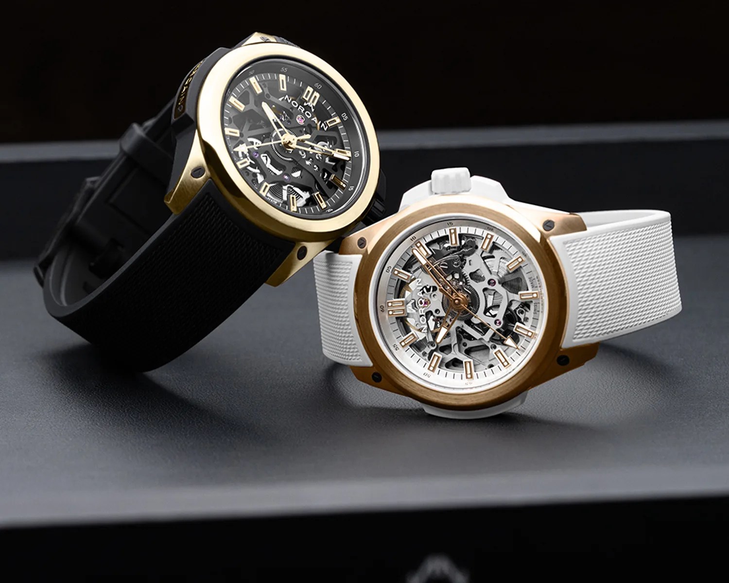 Two Norqain skeleton watches with gold-tone bezels, one with a black dial and black strap, the other with a white dial and white strap.